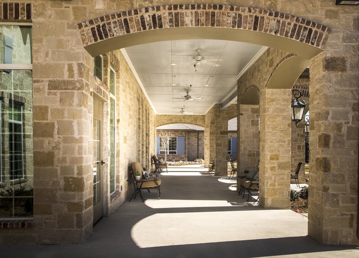 A sunlit stone corridor with arched ceilings and columns, casting shadows along the pathway.