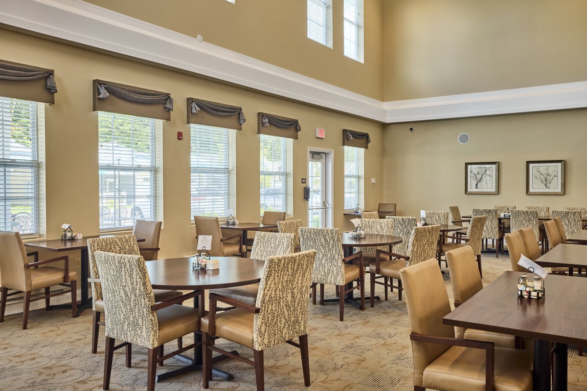 A spacious and well-lit dining room with several tables and chairs, featuring large windows.