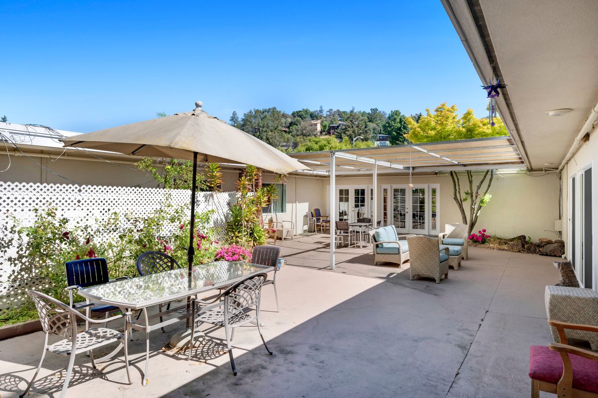 A spacious outdoor patio with comfortable seating, umbrellas, and a garden backdrop on a sunny day.