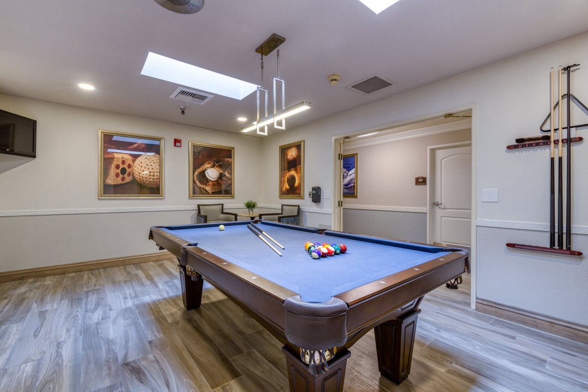 A stylish game room featuring a pool table with vibrant blue felt, framed artwork on the walls, and a modern hanging light fixture.