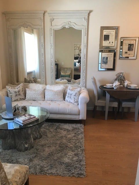 A cozy living room with a plush sofa, decorative pillows, and a glass coffee table, adjacent to a small dining area.