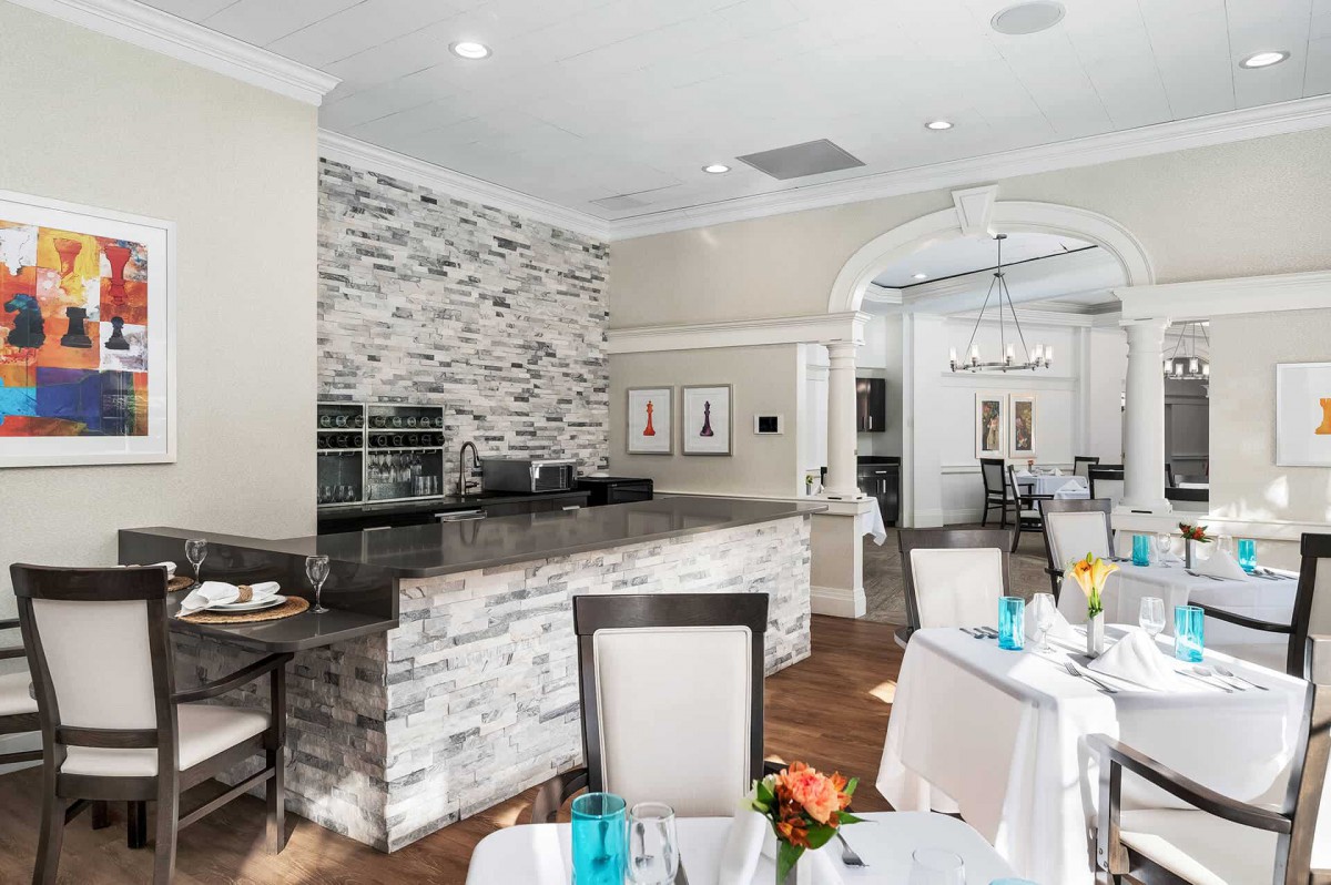 A modern restaurant interior with a stone-accented bar and elegantly set dining tables.
