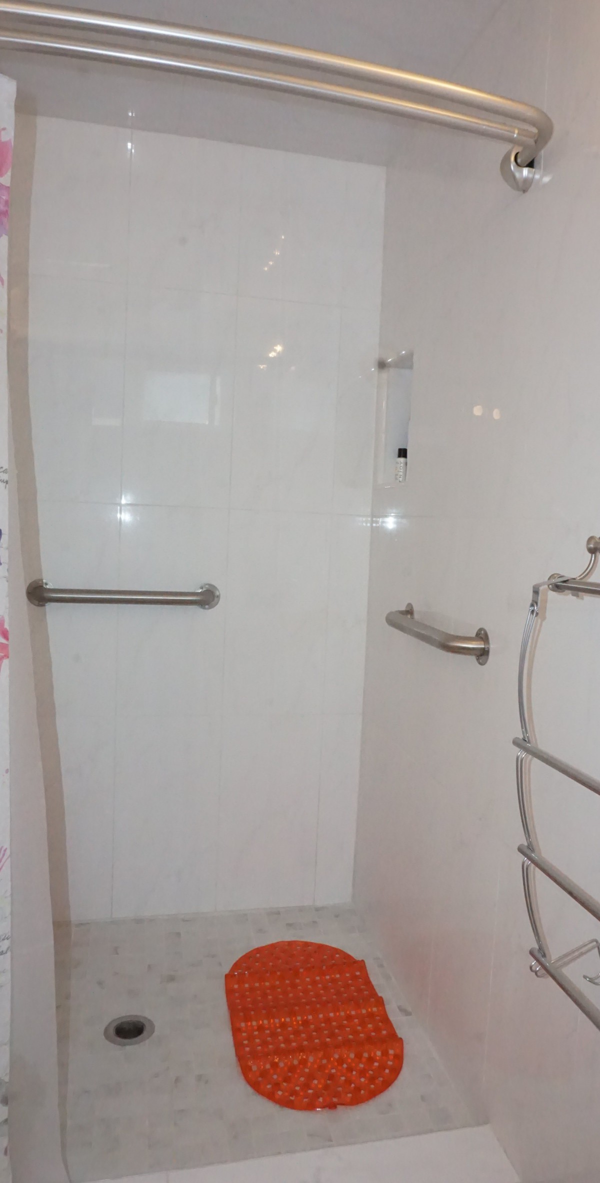 A bathroom shower area with white tiles, equipped with grab bars and a towel rack.
