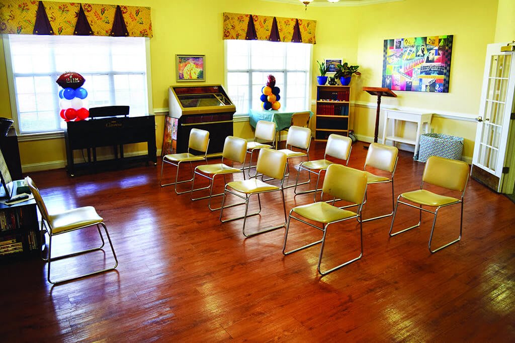 A small classroom setup with chairs arranged for a lecture, featuring a wooden floor and windows letting in natural light.