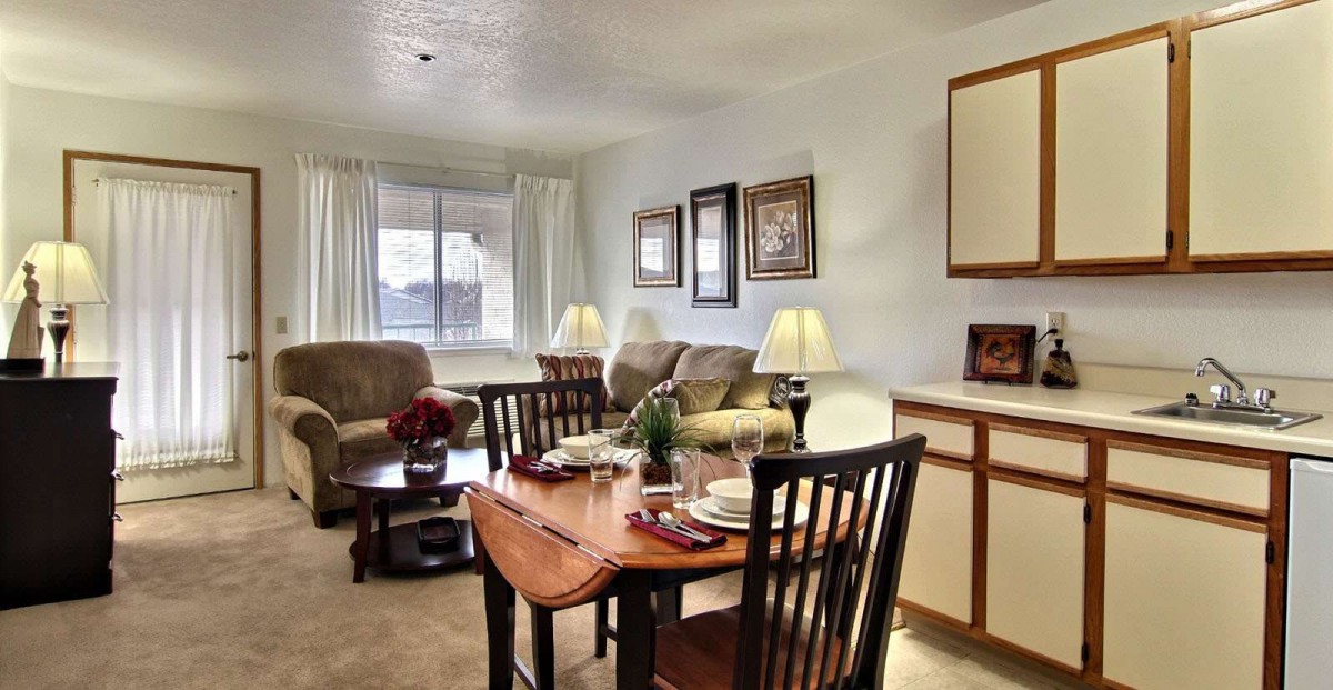 A cozy living room with a dining area, featuring comfortable sofas and a wooden dining set near a large window.