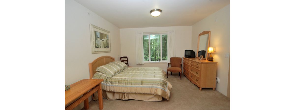 A cozy bedroom featuring a bed, dresser, and chair with a window view.