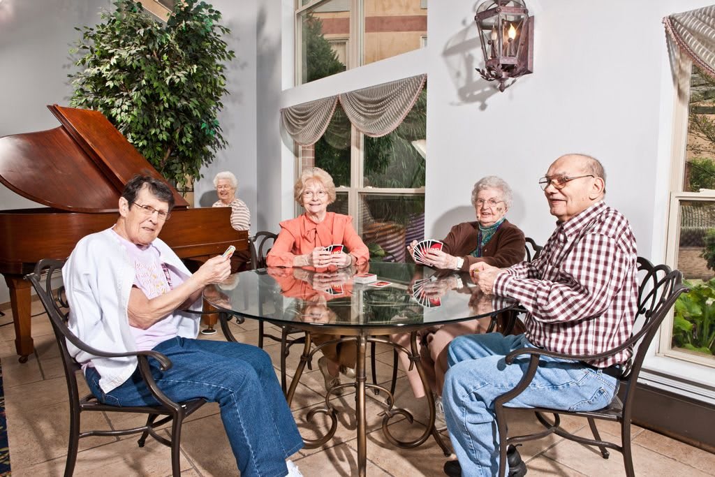 A group of seniors enjoying a card game indoors around a glass table.