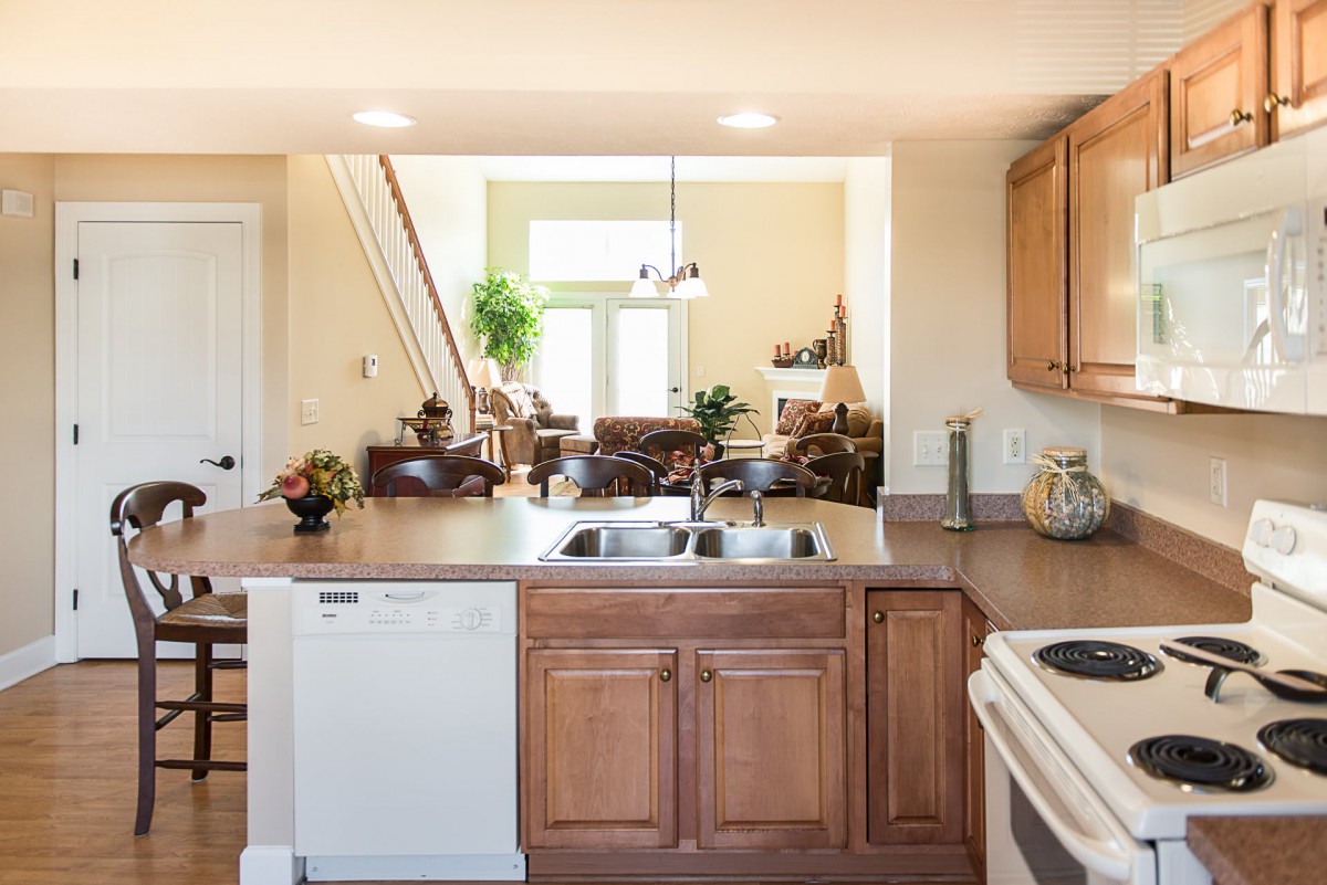 A modern kitchen with wood cabinetry opens into a bright living area.