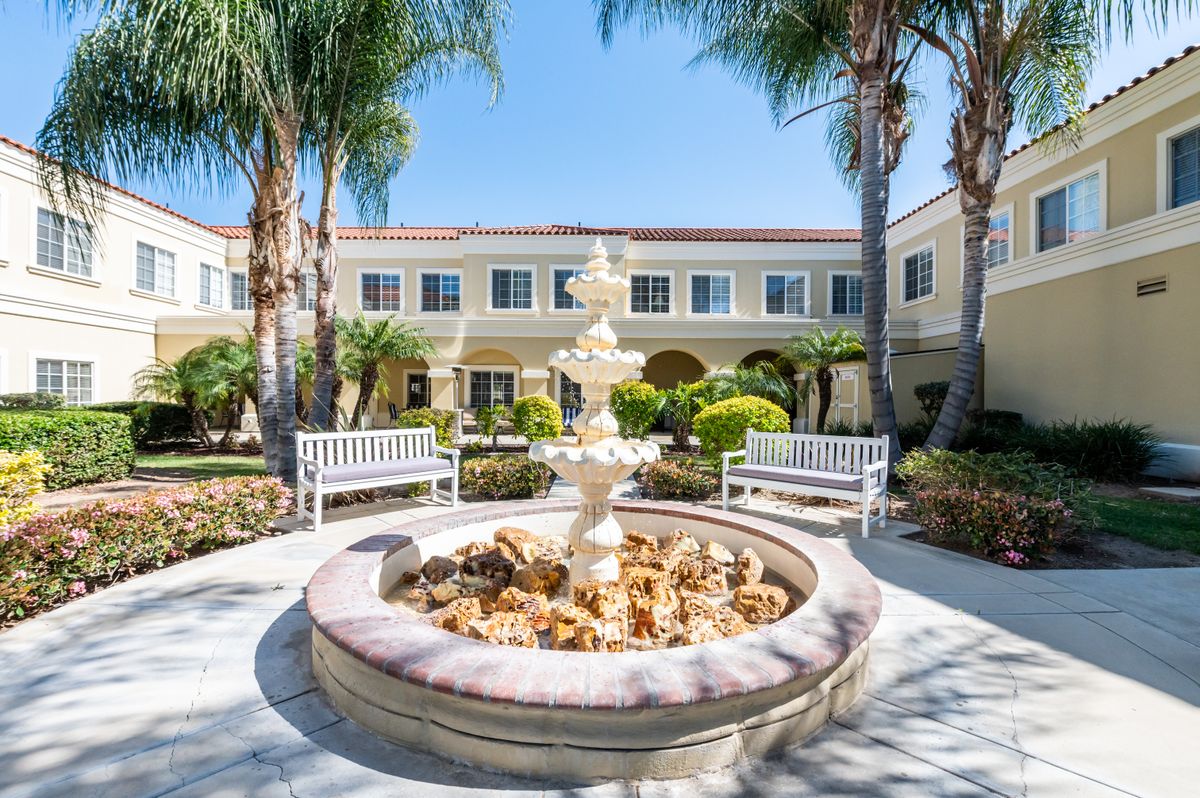 A serene courtyard featuring a central fountain surrounded by benches and palm trees.