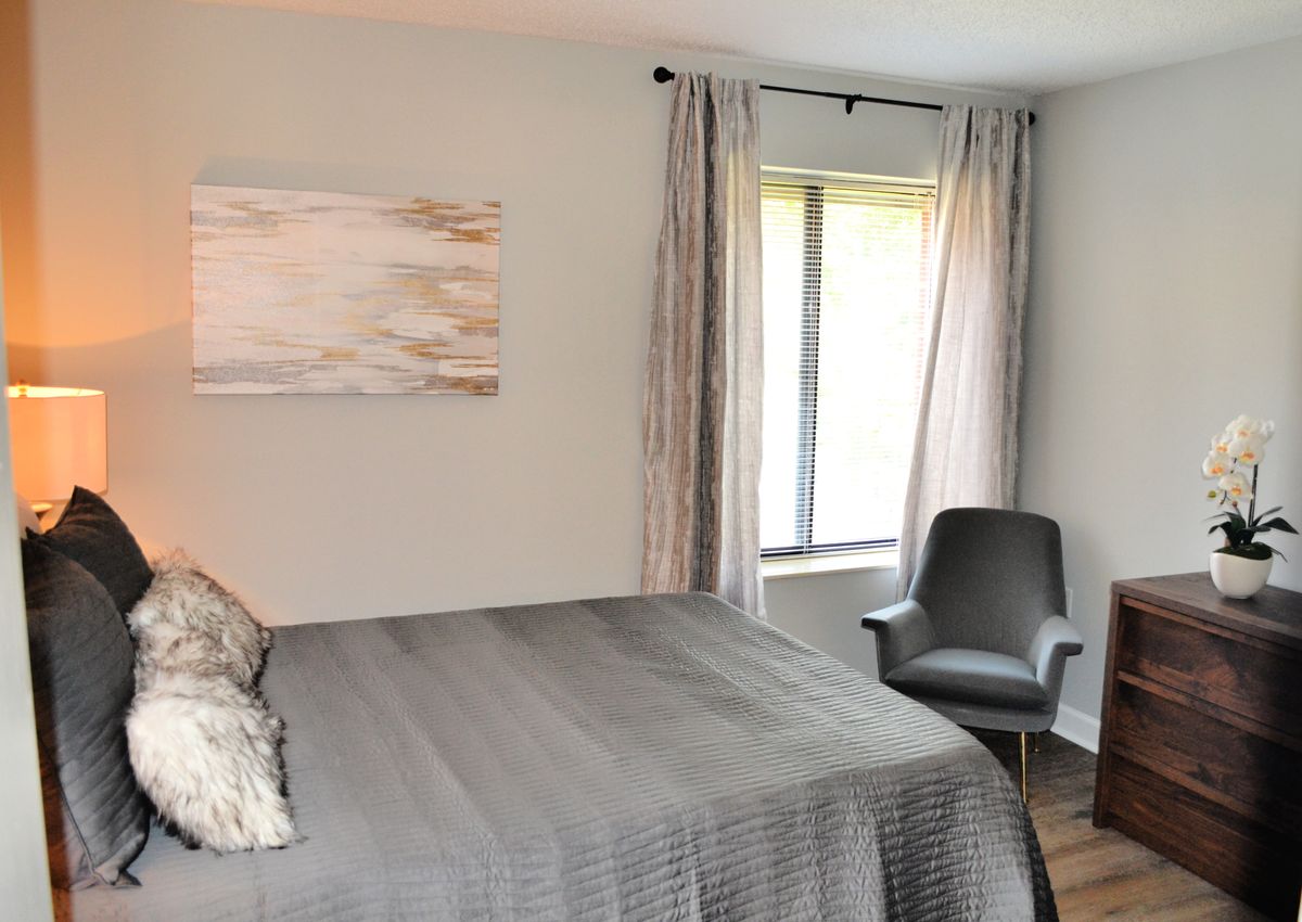A cozy bedroom with a neatly made bed, modern chair, and window with curtains.