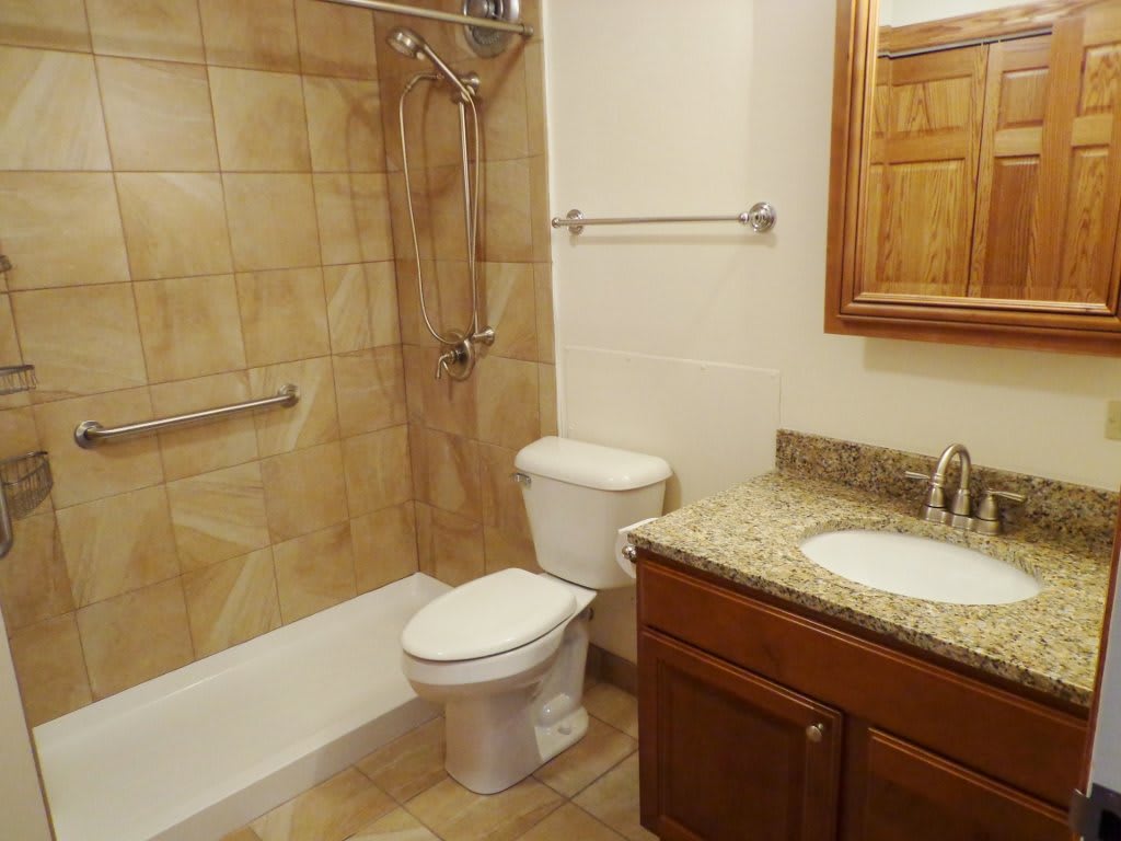 A clean and modern bathroom with a shower, toilet, sink, and mirror.