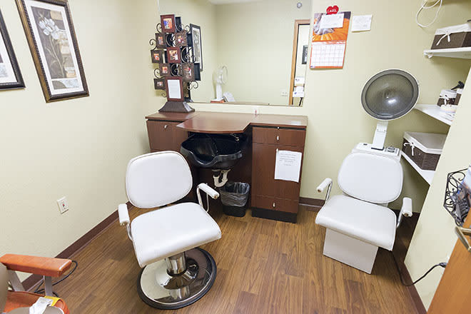 A cozy salon space featuring a styling chair, a mirror, and a hair dryer chair on a wooden floor.