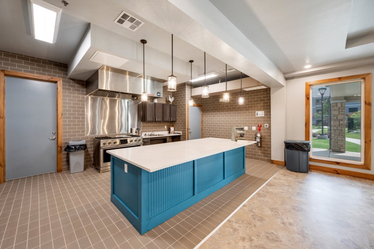 A modern kitchen featuring a blue island with pendant lighting and stainless steel appliances.