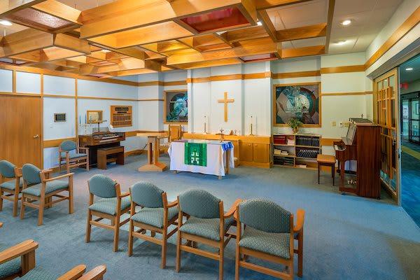 A serene chapel interior with chairs arranged for worship, featuring an altar and a prominent cross.