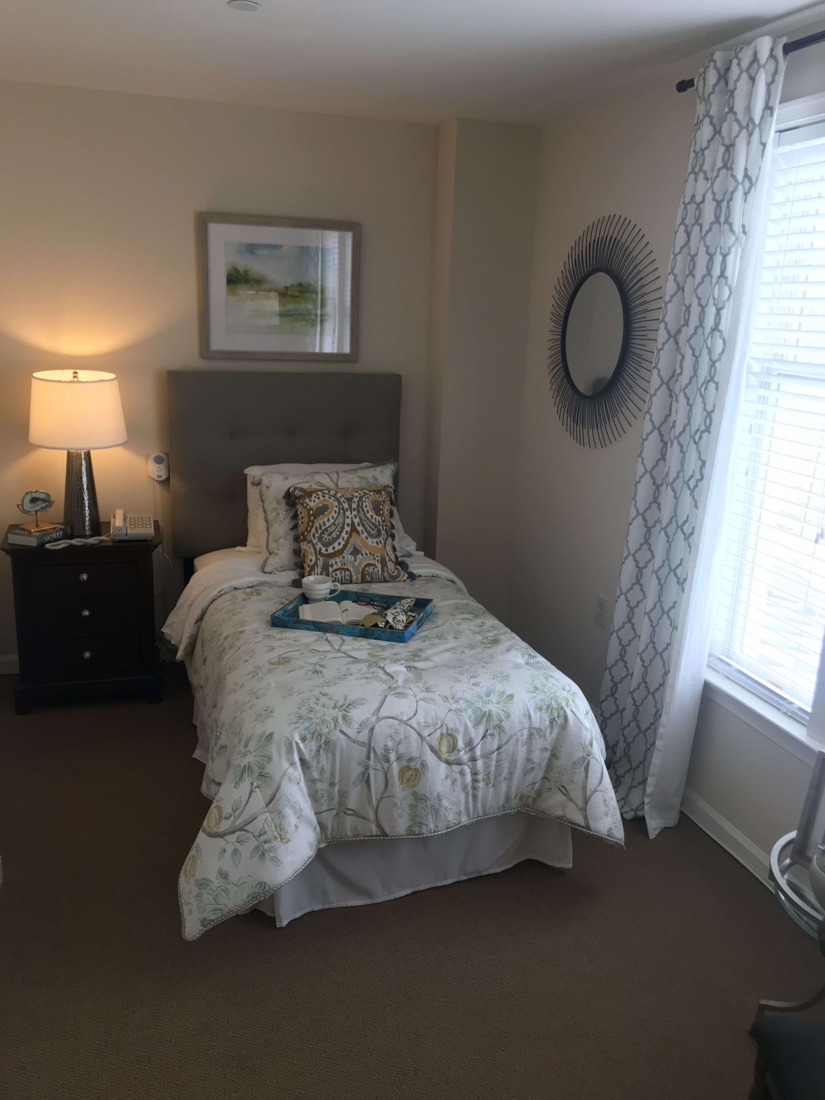 A cozy bedroom with a single bed, decorated with patterned bedding and illuminated by a bedside lamp on the nightstand.