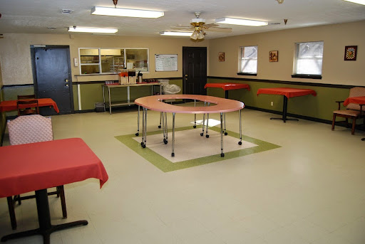 A spacious room featuring multiple tables, a kitchenette area, and bright lighting.
