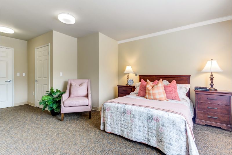 A cozy bedroom featuring a bed with decorative pillows, a bedside lamp, and an upholstered chair.