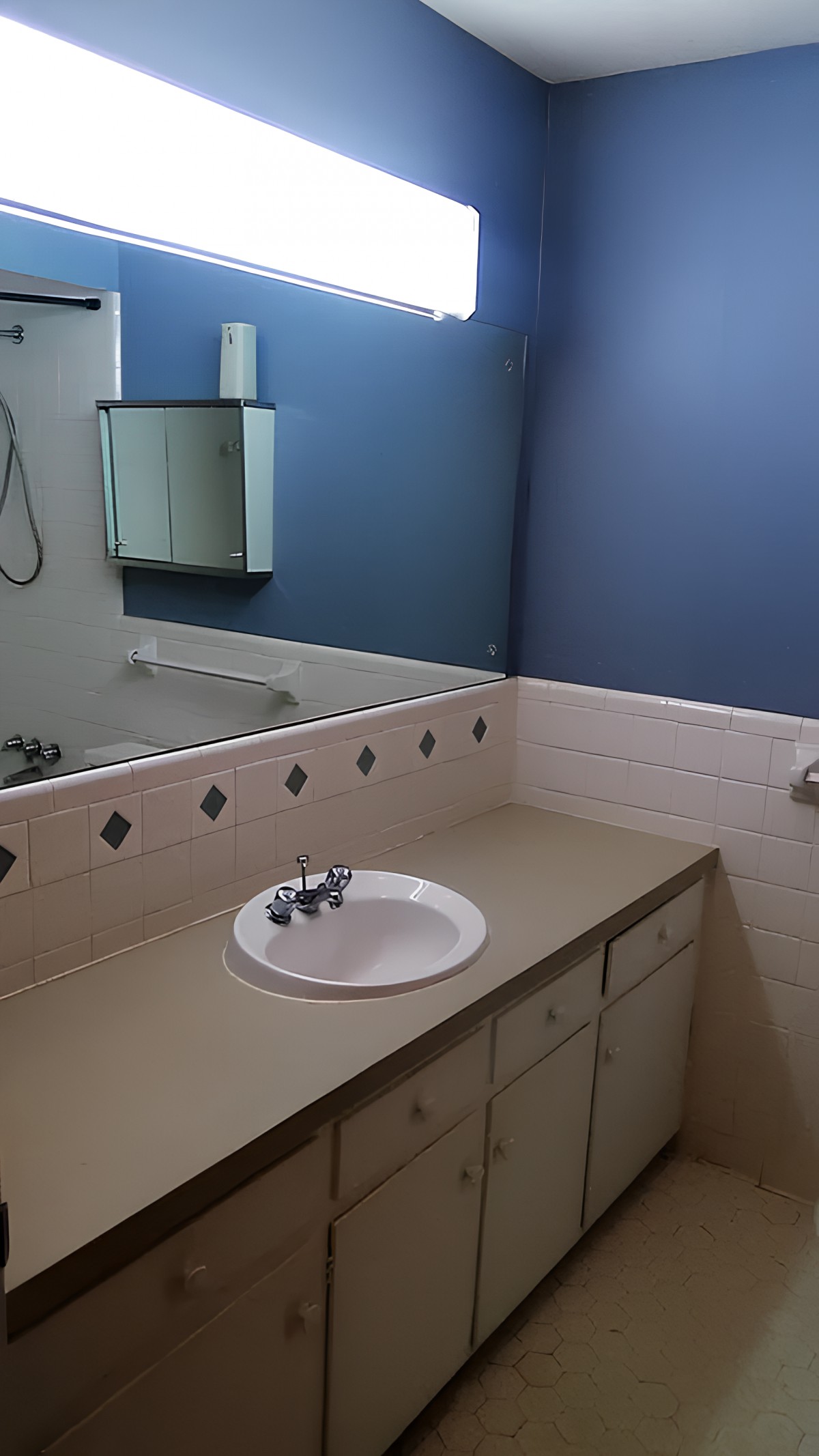 A clean bathroom with a countertop, sink, and mirror against a blue wall.