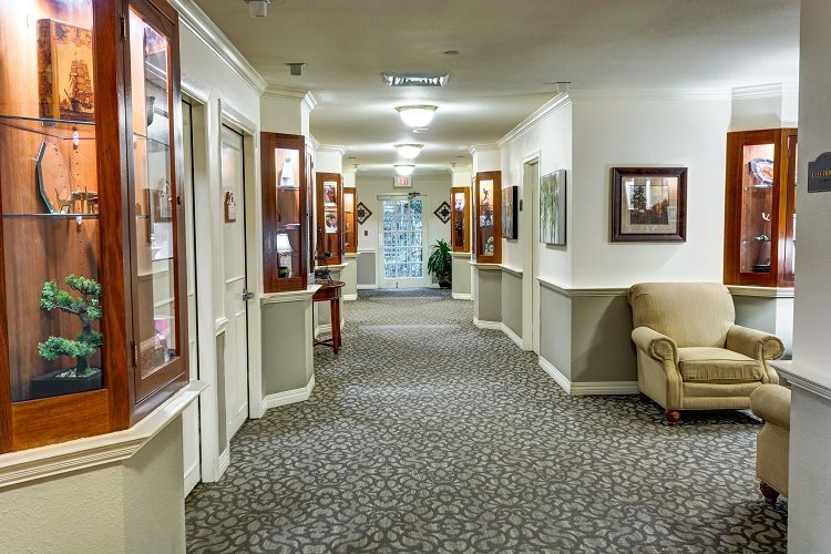 A well-lit hallway with carpet flooring and framed pictures on the walls.