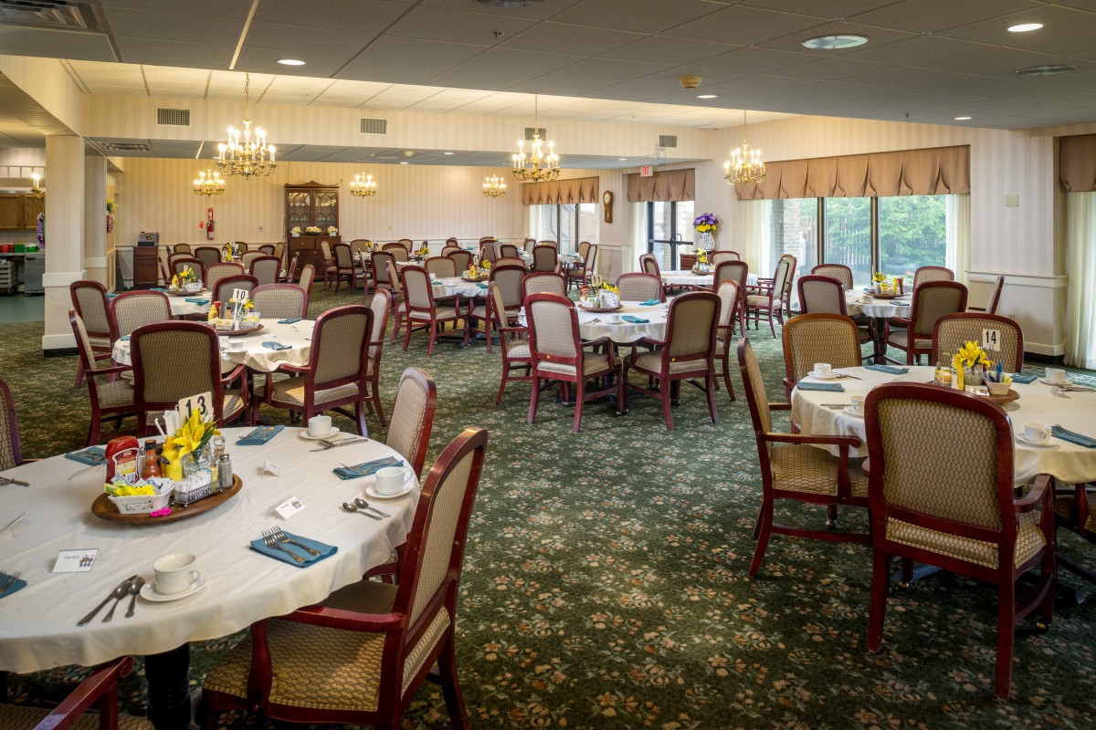 Elegant dining room with arranged tables and chairs, featuring chandeliers and a carpeted floor.