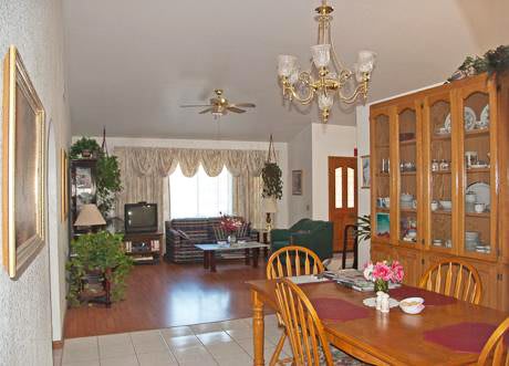 A cozy living and dining area with wooden furniture, decorative plants, and a chandelier.