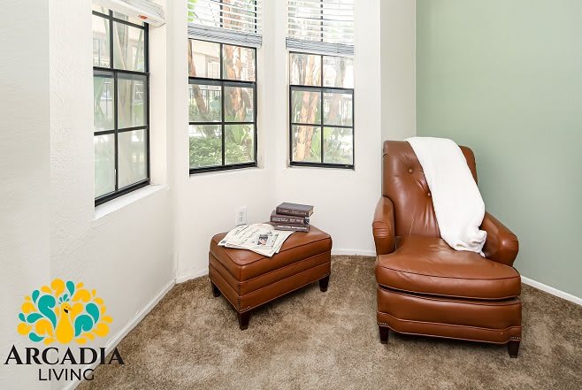 A cozy reading nook with a leather armchair and footstool beside large windows.