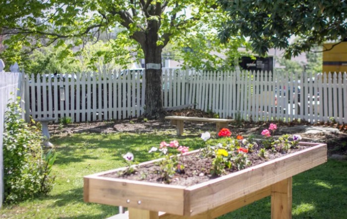 A backyard with a raised flower bed and white picket fence on a sunny day.