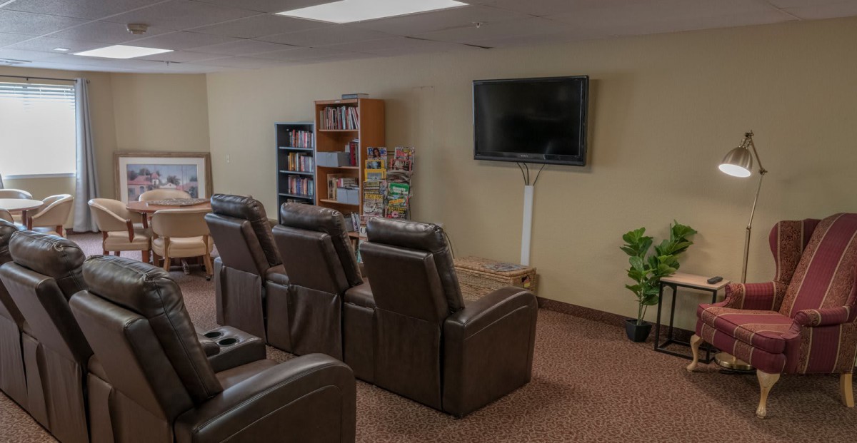 A cozy home theater setup with recliner chairs facing a wall-mounted TV and a bookshelf in the background.