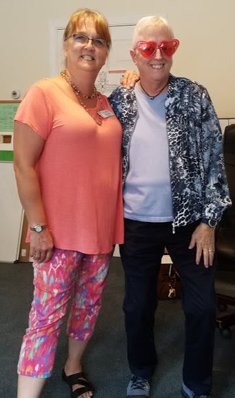 Two people standing side by side indoors, wearing casual clothing.