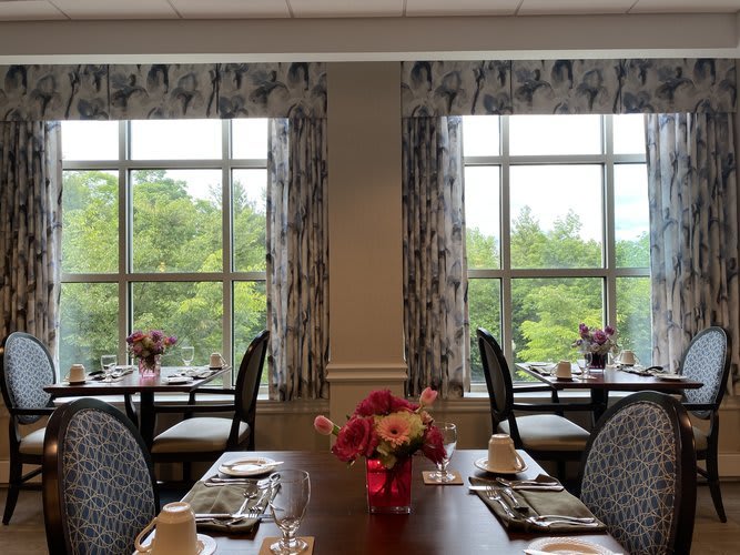 A well-decorated dining room with tables set for a meal, featuring large windows and floral centerpieces.