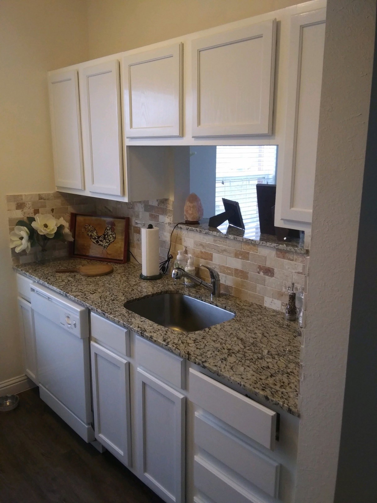 A modern kitchen with white cabinets and a granite countertop, featuring a sink and decorative flowers.