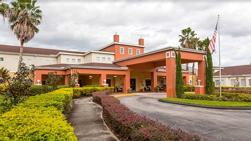 A large building with a covered entrance and landscaped surroundings under a cloudy sky.