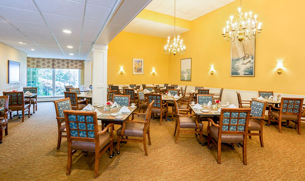 An elegant dining room interior with multiple tables and chairs, decorated with chandeliers and bright yellow walls.
