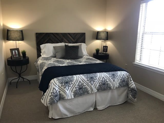 A cozy bedroom with a neatly made bed, featuring patterned bedding and pillows, illuminated by two bedside lamps.