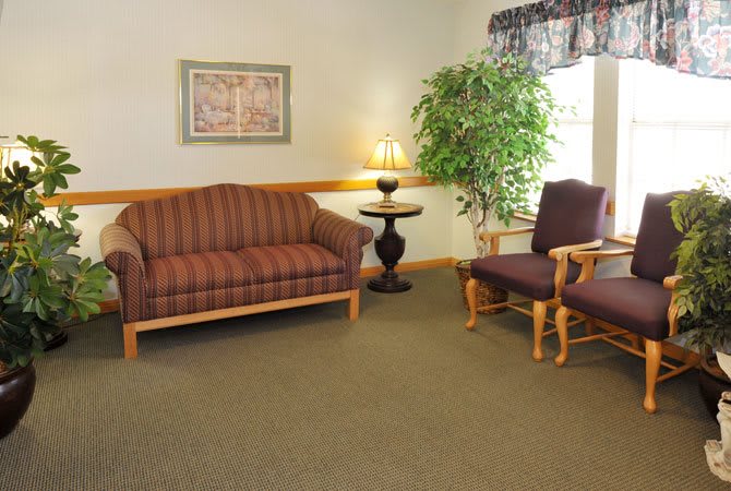 A cozy living room setup with a striped sofa, two chairs, a lamp on a small table, and an indoor plant.