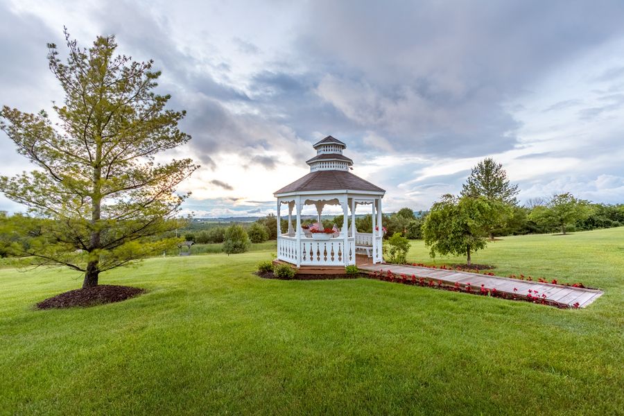 A scenic view of a gazebo surrounded by lush greenery and a cloudy sky.