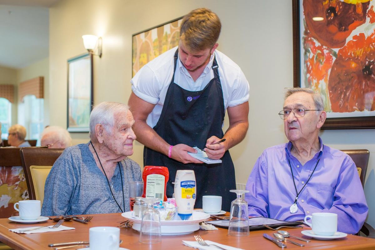 A waiter takes an order from two elderly men at a restaurant table.