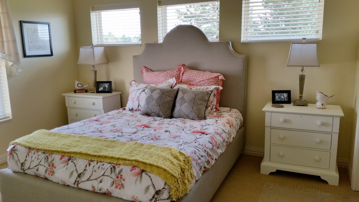 A cozy bedroom with a neatly made bed featuring floral bedding and decorative pillows, flanked by white nightstands and lamps.