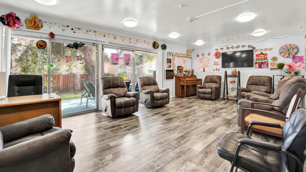 A cozy living room with recliner chairs, a piano, and a television, featuring wood flooring and a sliding glass door leading to the outside.