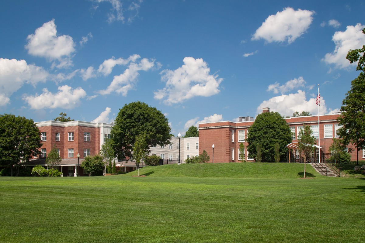 A scenic view of a college campus with brick buildings, a large grassy field, and a clear blue sky.