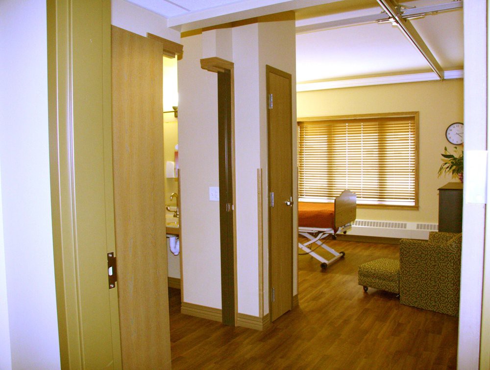 A view of a hospital room with a patient bed, furniture, and privacy curtains.
