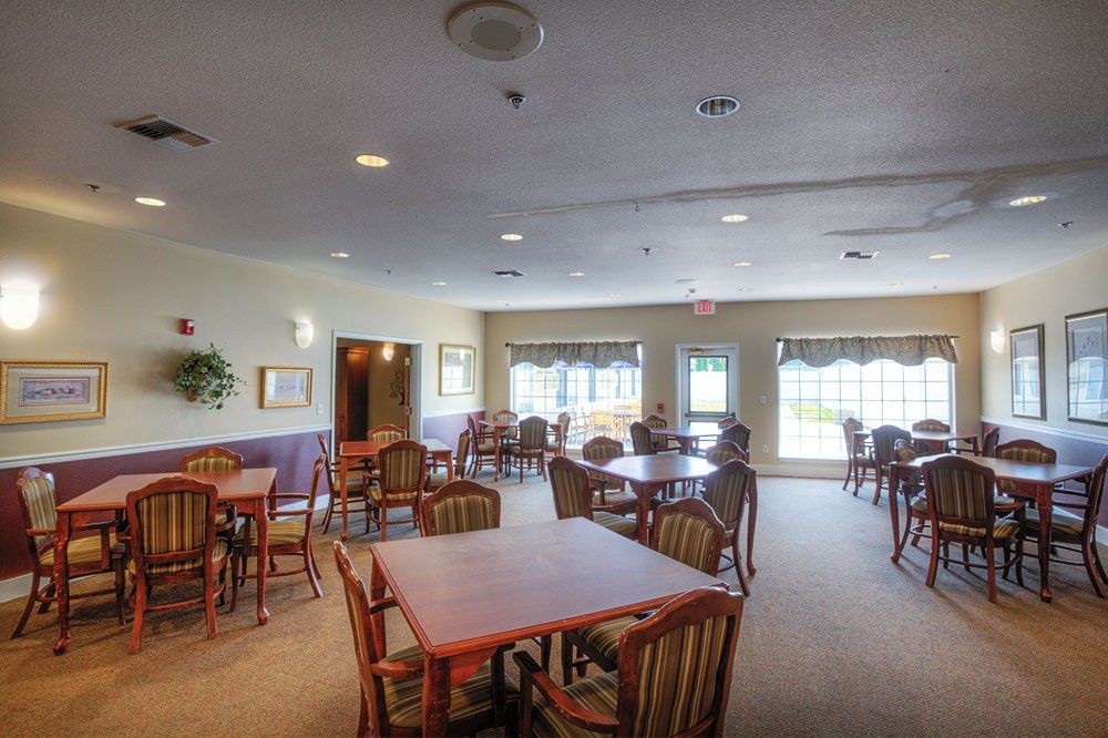 A spacious dining area with multiple tables and chairs, illuminated by natural light from large windows.