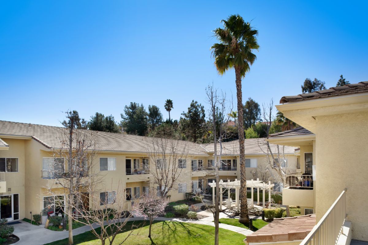 A sunny view of an apartment complex with a central courtyard and palm trees.