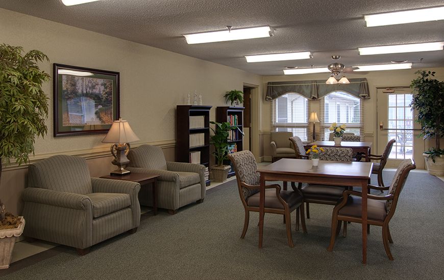 A cozy living room area with comfortable seating, a table, bookshelves, and large windows.