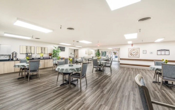 A spacious dining room with several tables and chairs, featuring hardwood flooring and bright interior lighting.