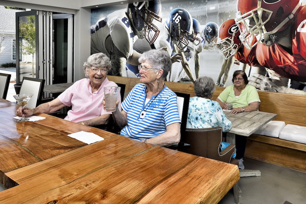 A group of elderly women enjoying a conversation in a dining room with a sports-themed mural.