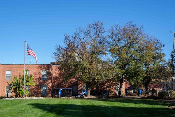 A brick building with an American flag in front, surrounded by trees and a green lawn under a clear blue sky.
