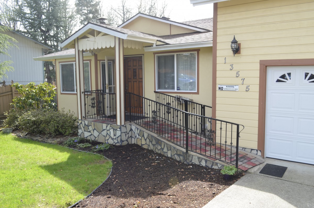 A yellow house with an accessible ramp leading to the front porch.