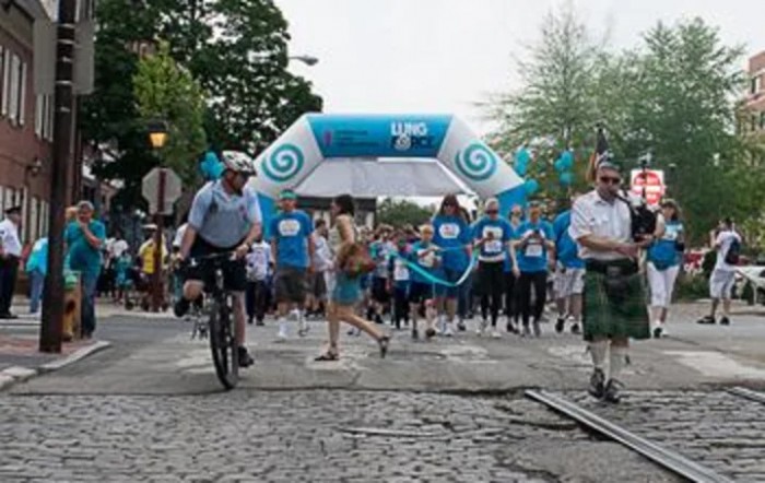 Participants gather at the starting line of a marathon event, with a cyclist passing by.