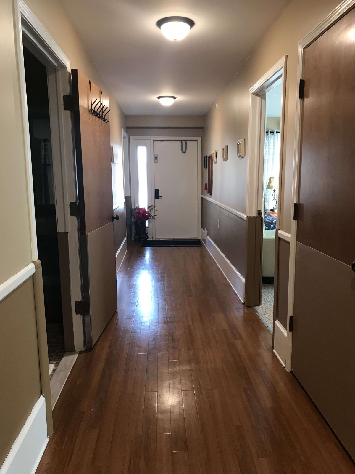 A well-lit residential hallway with wooden flooring and doors leading to various rooms.